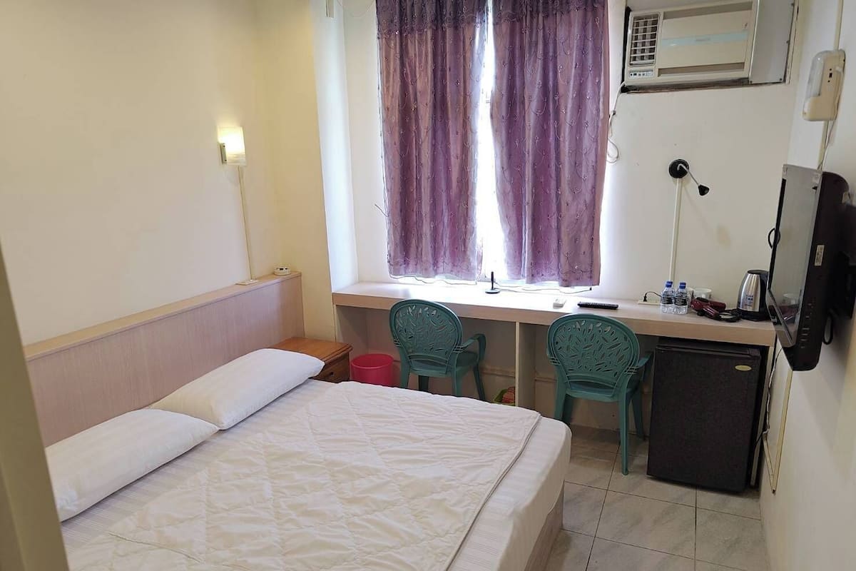 A hotel room with a bed, a desk with two chairs, a small refrigerator, and a television.