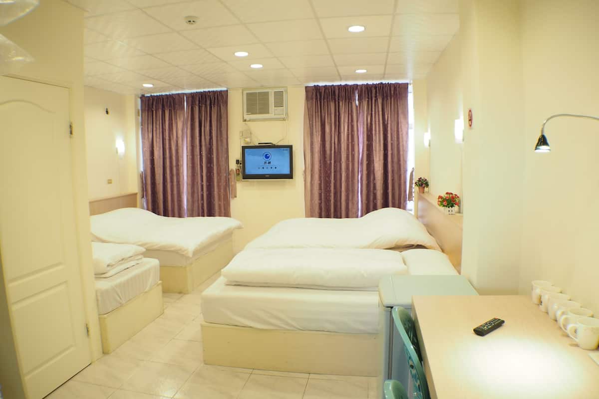 A hotel room with two beds, a TV, a desk with a remote, and a wall-mounted air conditioner.