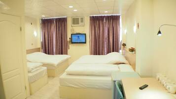 A hotel room with two beds, a TV, a desk with a remote, and a wall-mounted air conditioner.