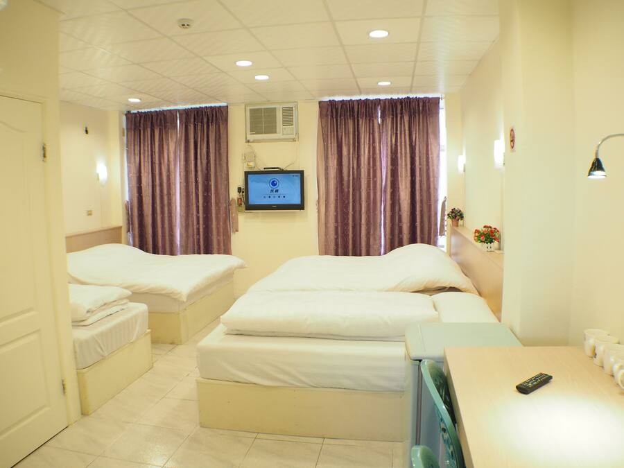 A hotel room with two beds, a TV, a desk with a remote, and a wall-mounted air conditioner.