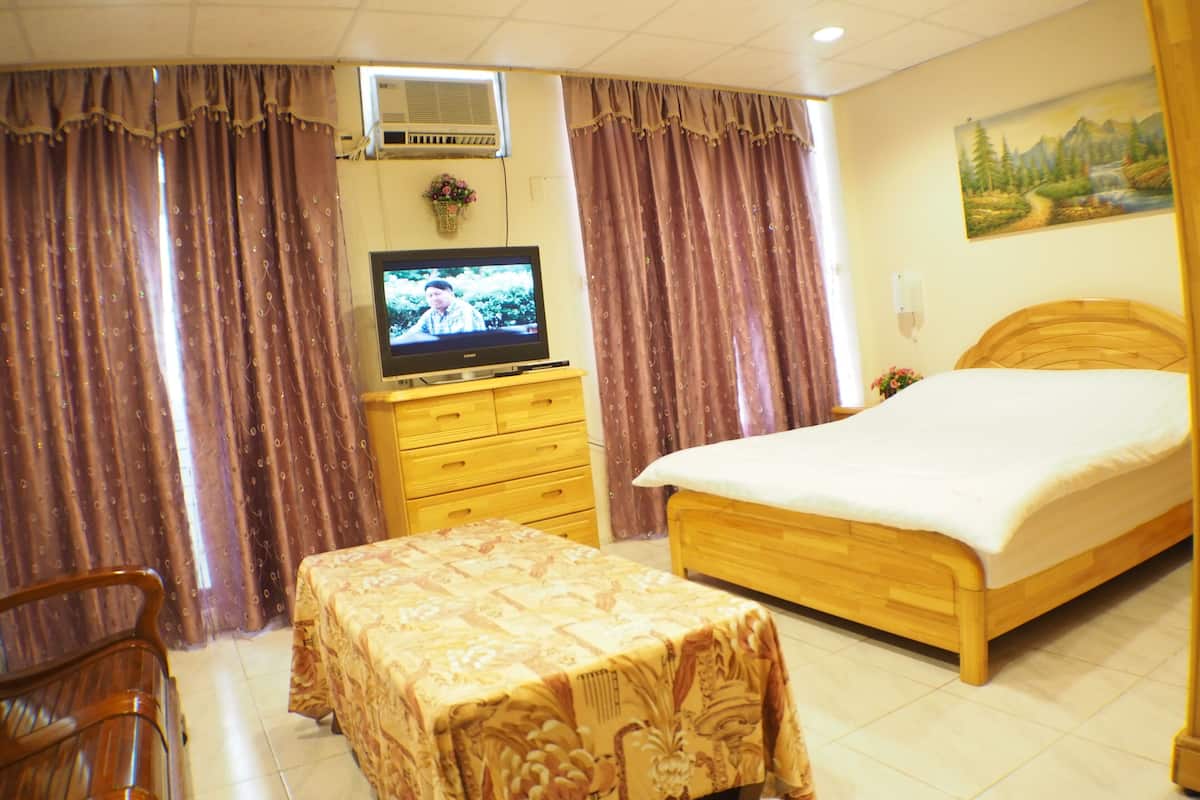 A hotel room with a bed, a TV on a wooden cabinet, a small table with a tablecloth, and curtains.
