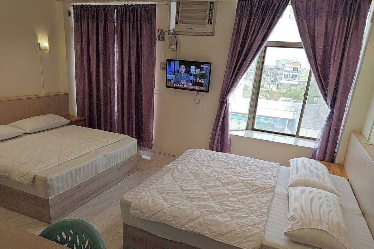 A hotel room with two beds, a TV, and a window with curtains.
