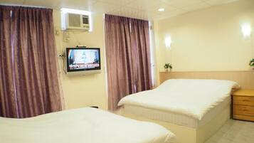 A hotel room with two beds, a television, an air conditioner, and curtains.