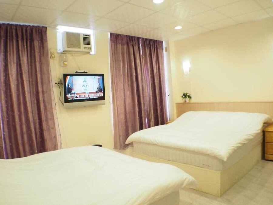 A hotel room with two beds, a television, an air conditioner, and curtains.