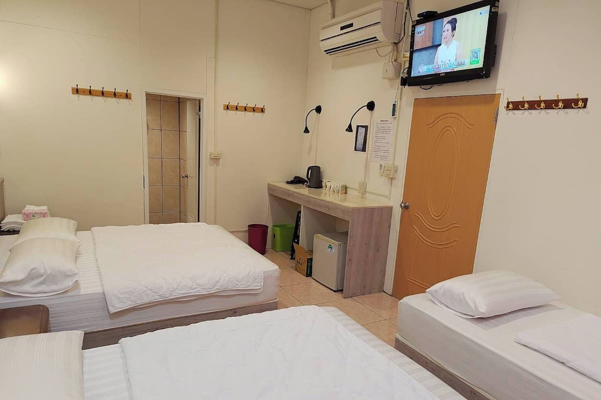 A hotel room with two beds, a desk with a computer, a small fridge, and a TV mounted on the wall.