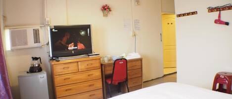 A hotel room with a bed, a wooden dresser, a television, a desk, and a chair.