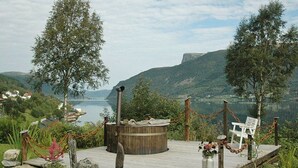 A wooden deck with a hot tub, surrounded by rocks and plants, overlooking a lake and hills. - 4 Star Holiday Home in Syvde (Vanylven)