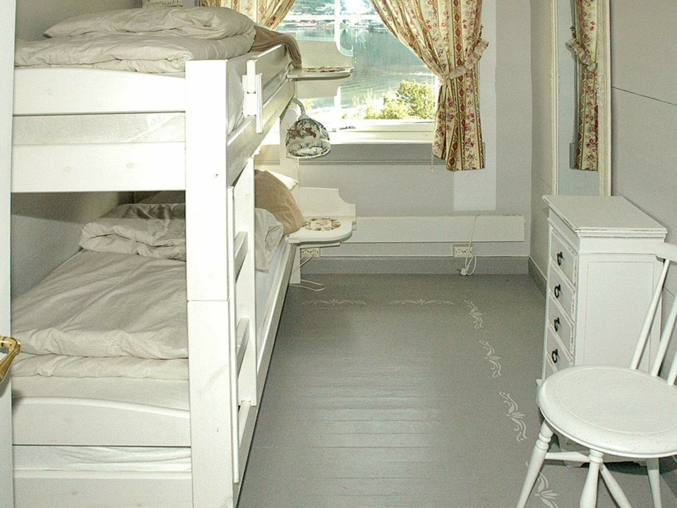 A small, compact room with bunk beds, a small table, a chair, and a window with curtains.