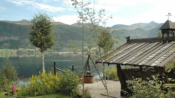 A rustic cabin with a metal roof and a small tower, surrounded by lush greenery and a lake. - 4 Star Holiday Home in Syvde (Vanylven)