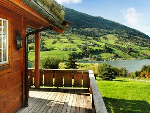 A wooden cabin with a porch overlooking a lake and rolling hills. - 4 Star Holiday Home in Olden (Stryn)