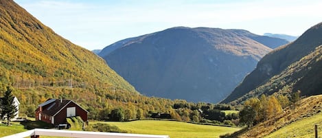 Paisaje rural con una terraza de madera, un pequeño edificio rojo y un valle con montañas al fondo.