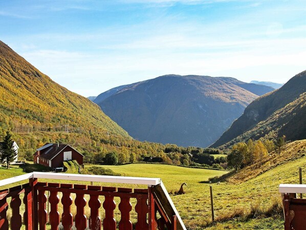 A rural landscape with a wooden deck, a small red building, and a valley with mountains in the background.