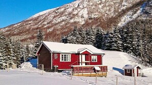 A red cabin with a porch and a small adjacent shed, surrounded by snow-covered trees and a mountain. - 6 Person Holiday Home in Ovre Ardal (Ardal)
