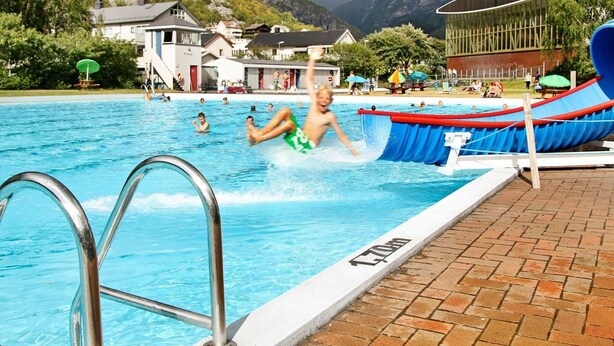 A swimming pool with a slide, surrounded by houses and mountains. - 6 Person Holiday Home in Ovre Ardal (Ardal)