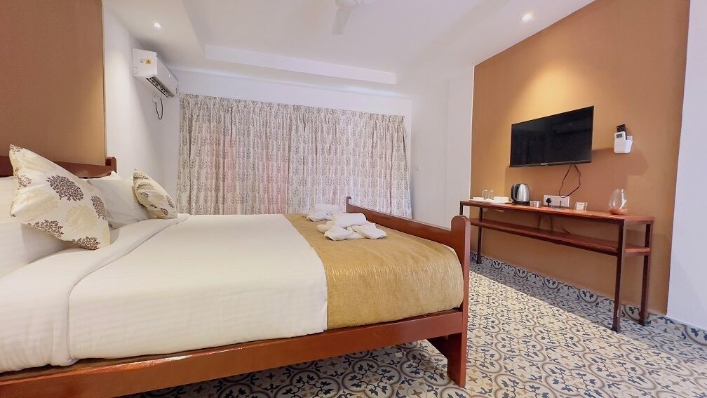 A hotel room with a bed, a desk, a television, and a patterned floor.