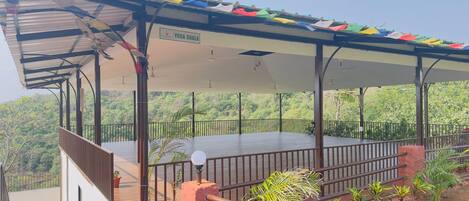A covered outdoor area with a wooden deck, a railing, and a view of a forested hillside.