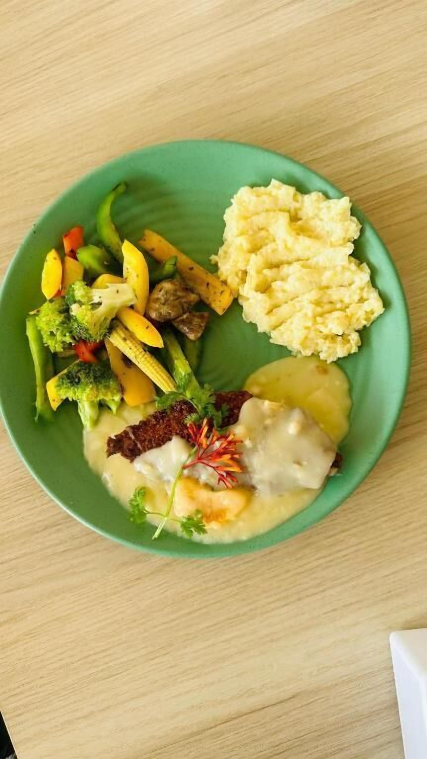 Un plato con huevos revueltos, puré de papas y una variedad de vegetales, incluyendo brócoli, zanahorias y maíz.