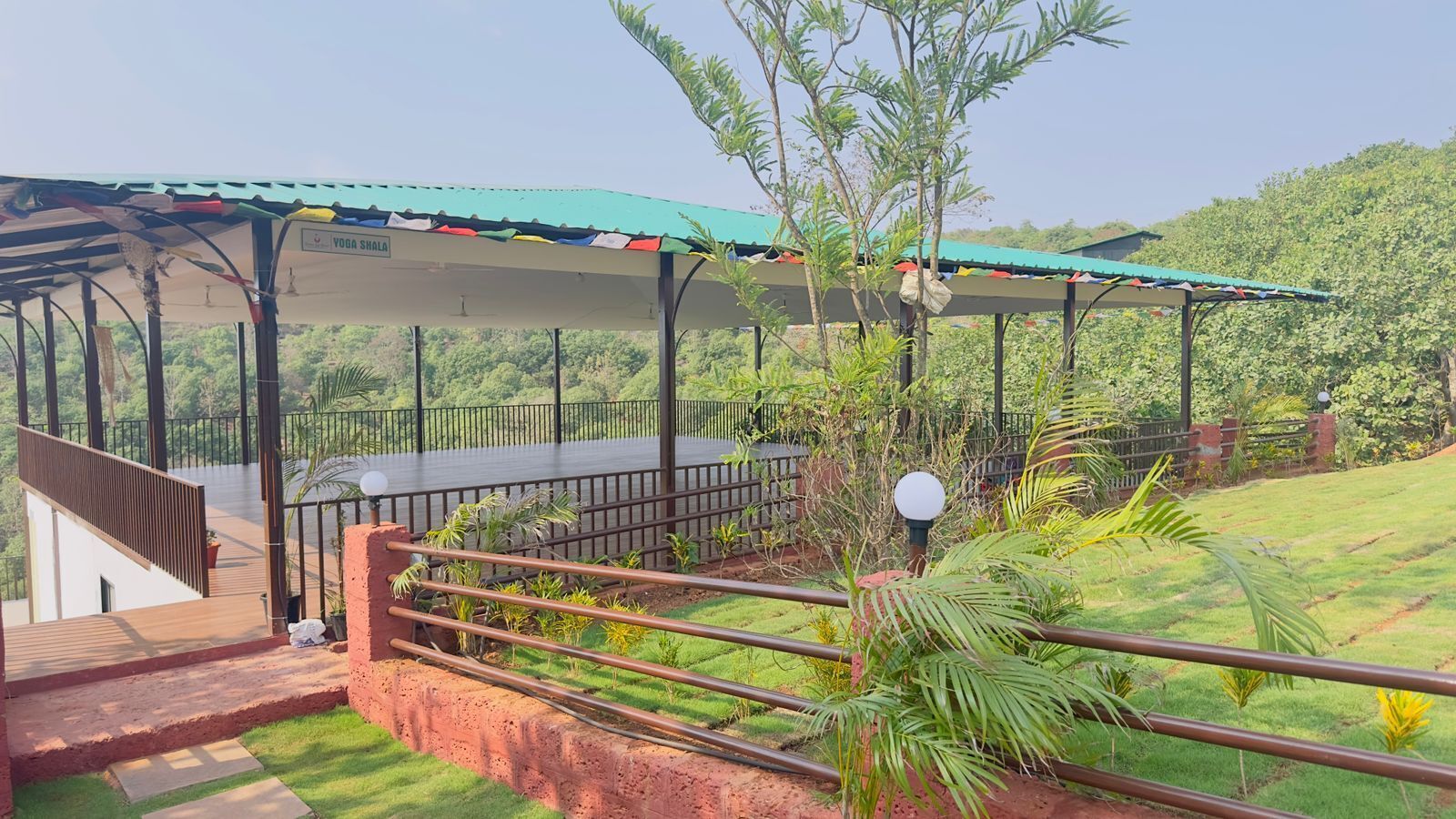 A covered outdoor area with a wooden deck, a metal railing, and a view of a lush green landscape.