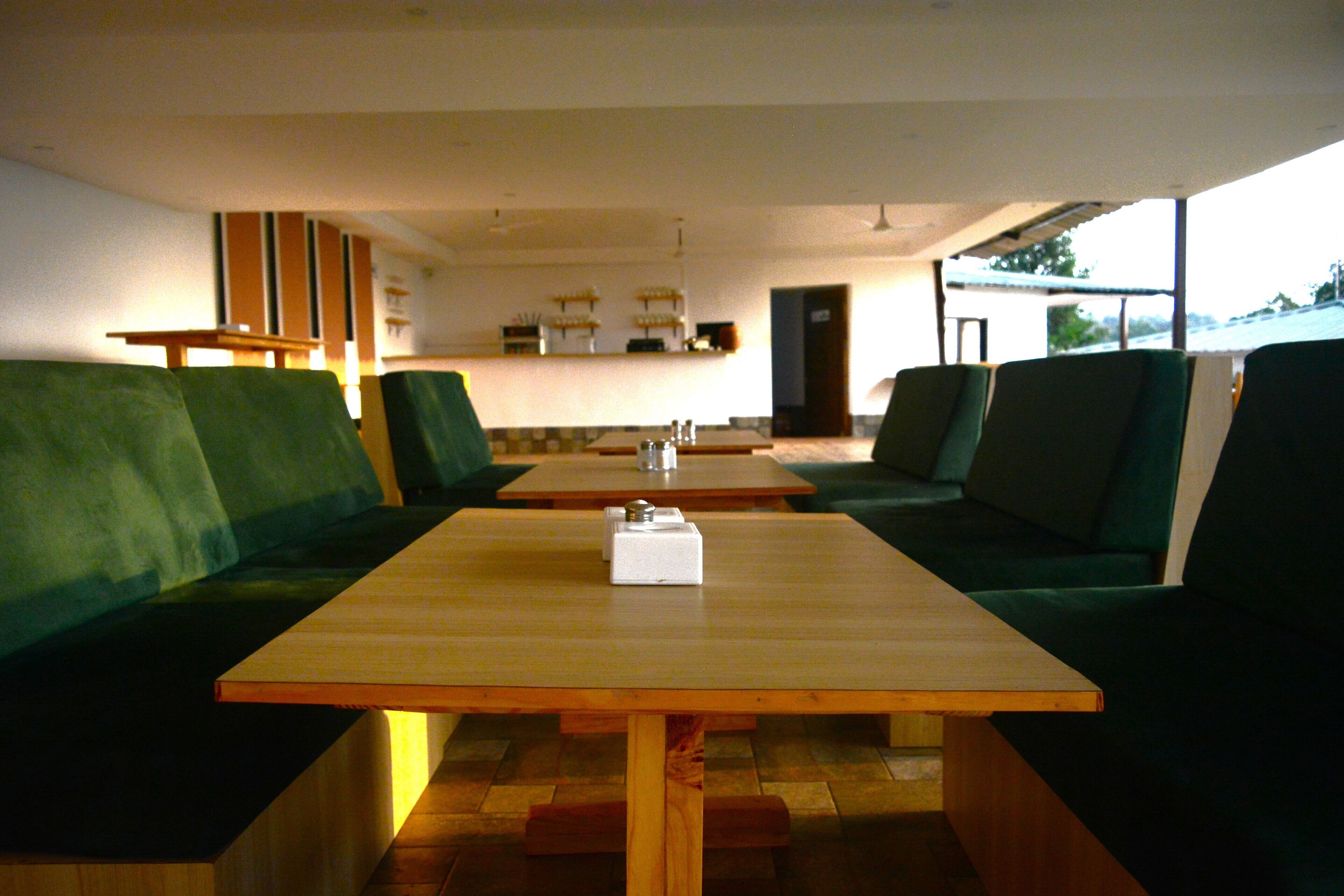 Un espace repas avec des banquettes et des tables, un plancher en bois et une vue sur l’extérieur.