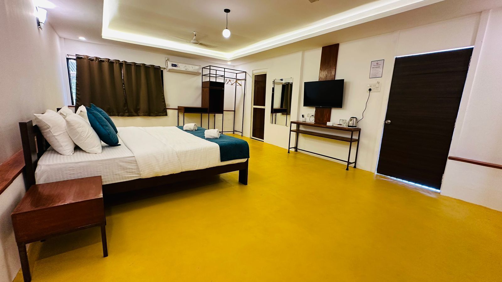 A hotel room with a bed, bedside table, a desk with a chair, a television, and a door.