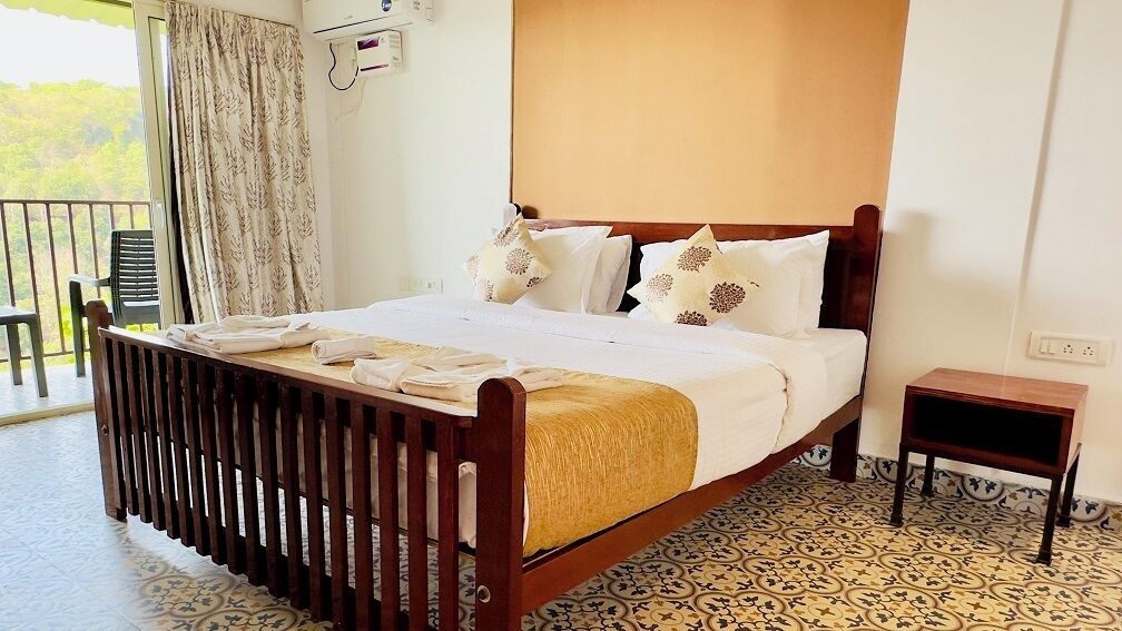 A neatly made bed with white linens and decorative pillows, a wooden headboard, a bedside table, and a patterned floor.