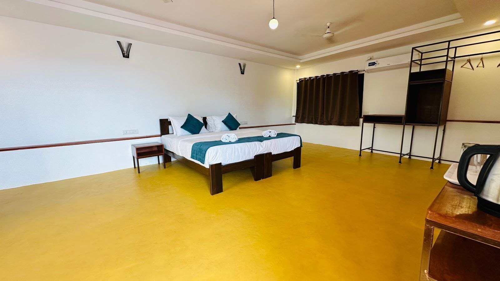 A room with a bed, a small table, a kettle, and a wardrobe.