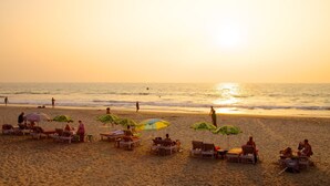 Une plage avec des transats et des parasols, un ciel dégagé et l’océan.