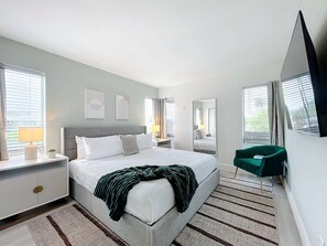 Ein modernes Schlafzimmer mit einem großen Bett, Nachttischen, einem Spiegel und Blick ins Freie durch die Fenster.