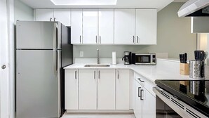 Una cocina moderna con gabinetes blancos, un refrigerador de acero inoxidable, un microondas y una estufa.