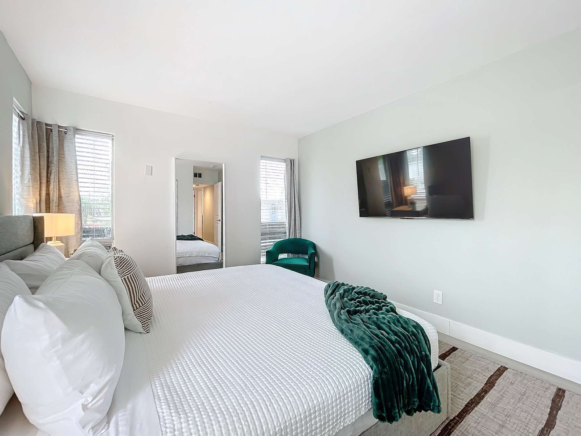A hotel room with a large bed, a TV mounted on the wall, and a view of the hallway.
