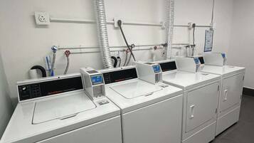 A row of white commercial washers with control panels, connected to a central ventilation system.