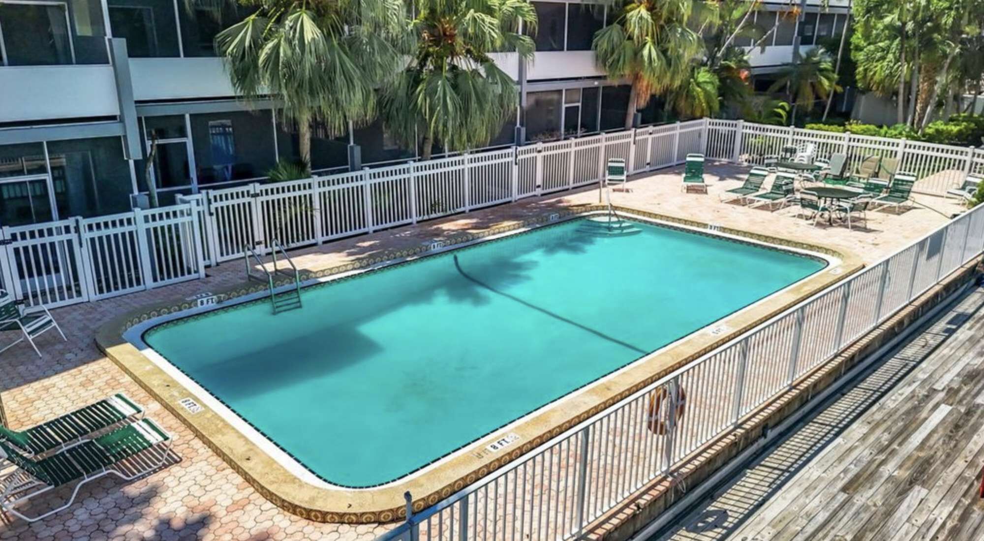 A rectangular pool with a white fence and lounge chairs.