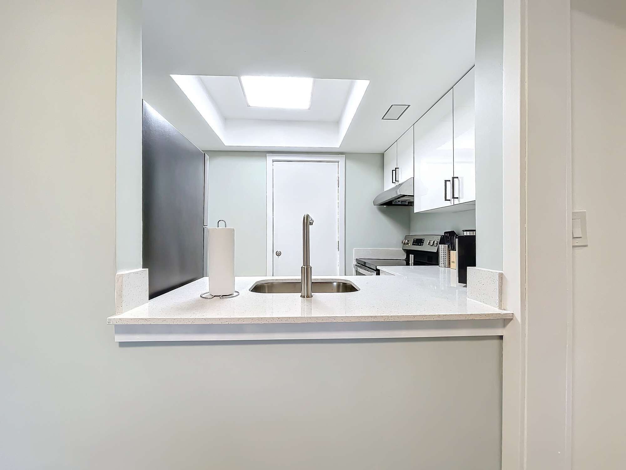 A modern kitchen with a skylight, stainless steel appliances, and white cabinetry.