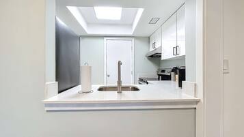 A modern kitchen with a skylight, stainless steel appliances, and white cabinetry.