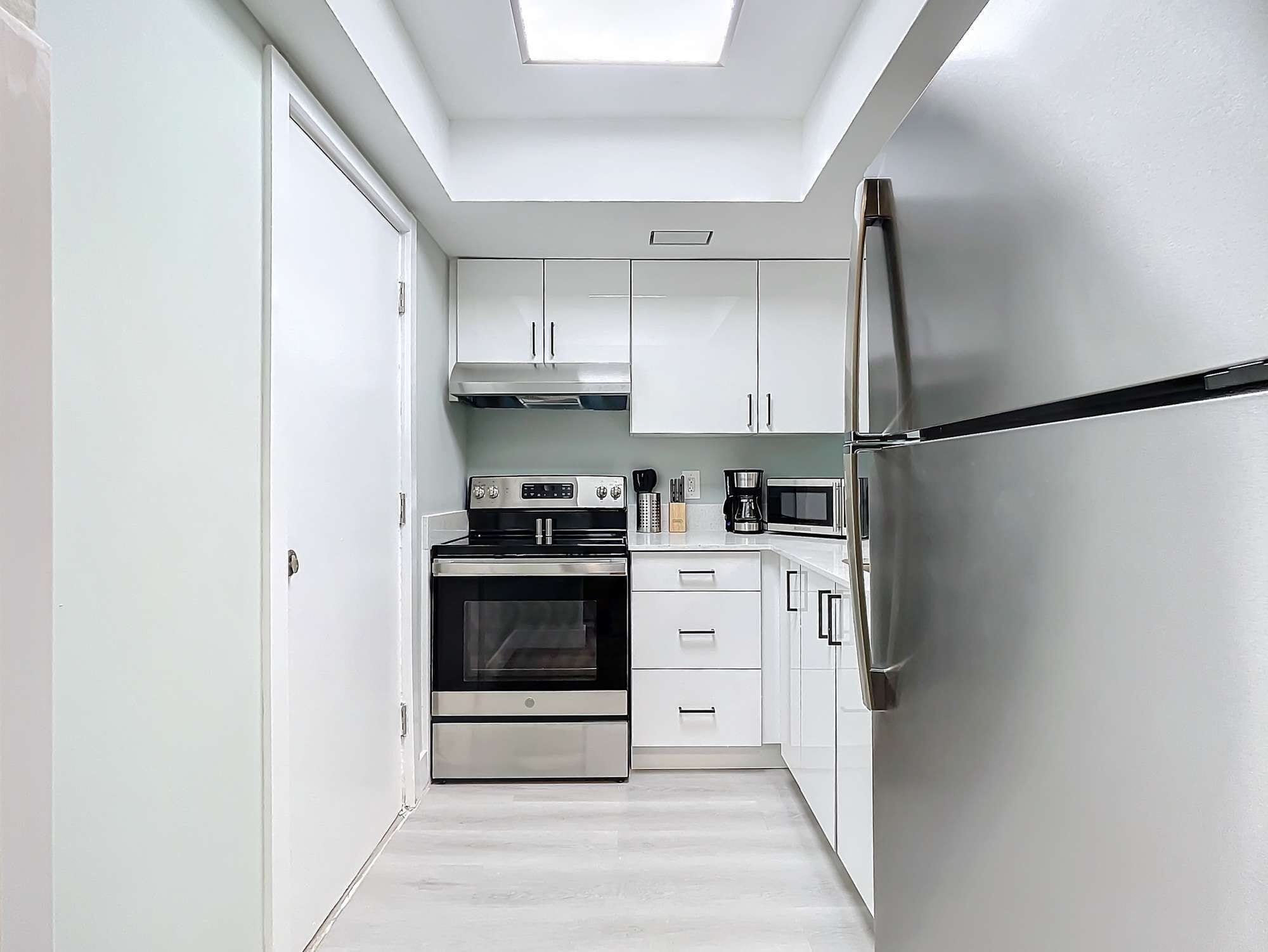 Una cocina moderna con armarios blancos, electrodomésticos de acero inoxidable y un tragaluz.