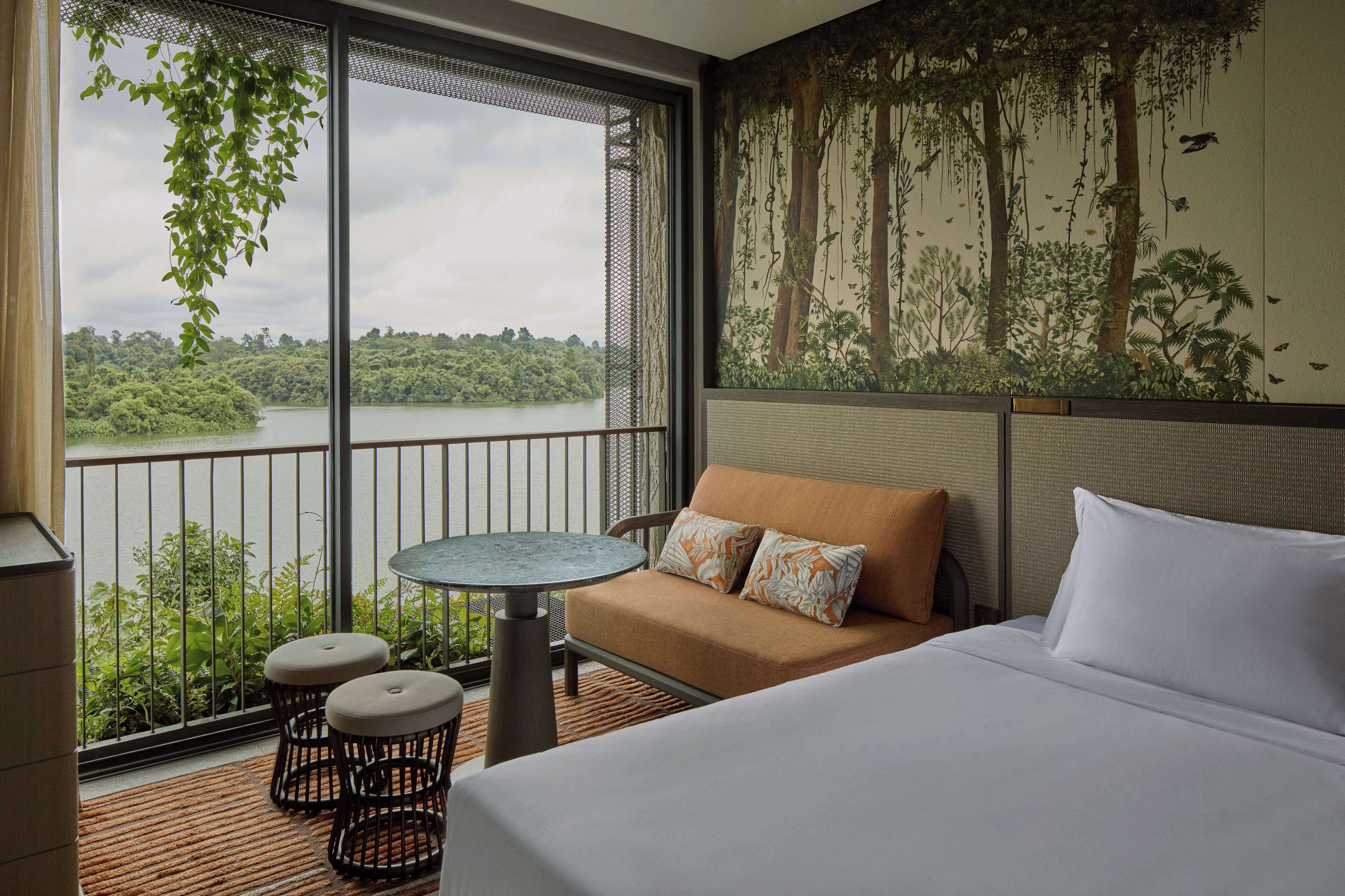A hotel room with a balcony, a bed, a sofa, a small round table, and two stools.