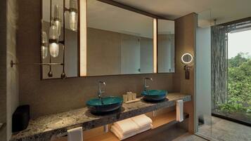A modern bathroom with two sinks, a large mirror, and a view of greenery outside.