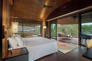 Une chambre moderne avec un grand lit, une table de chevet, une lampe et une vue sur l’extérieur grâce à de grandes fenêtres.