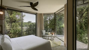 A bedroom with a bed, a ceiling fan, a balcony with a chair and table, and a view of greenery.