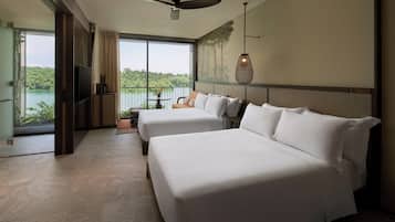 Habitación de hotel con dos camas, televisión, ventilador de techo y un amplio ventanal con vistas a un lago y vegetación.