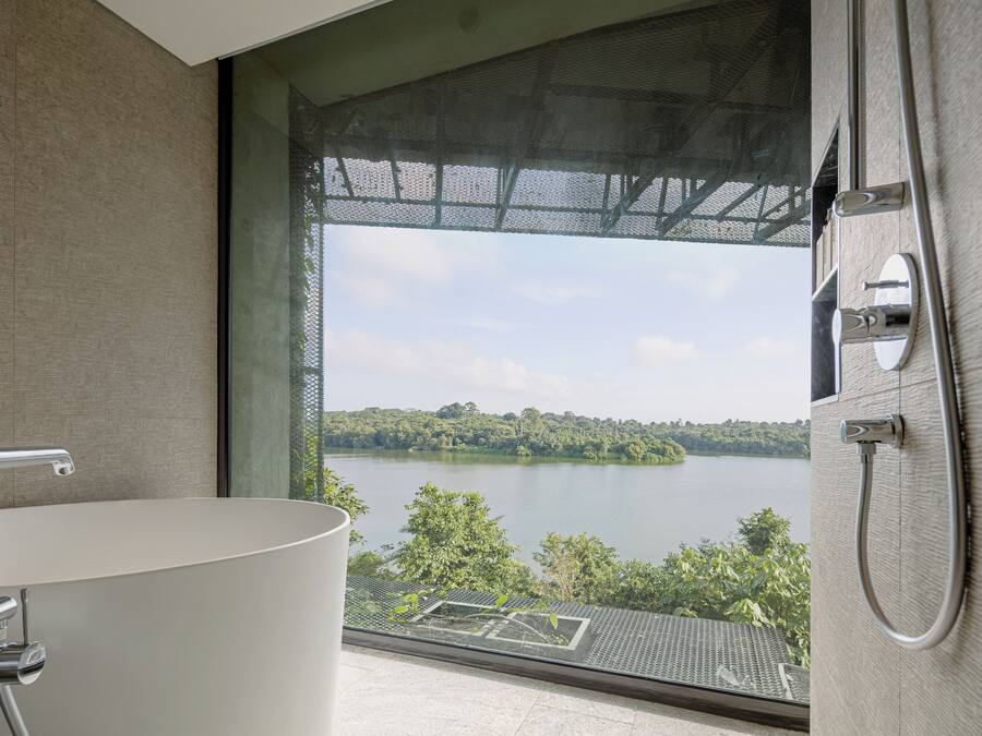 A modern bathroom with a bathtub, a shower, and a large window overlooking a lake.