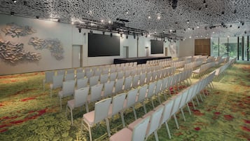 A conference room with rows of chairs, a stage with a black backdrop, and a ceiling with a unique lattice design.