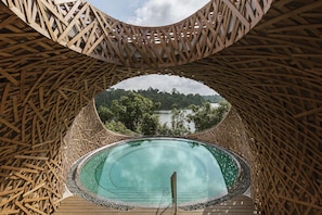 Une structure circulaire en bois, avec une piscine au centre, entourée d’un treillage en bois.