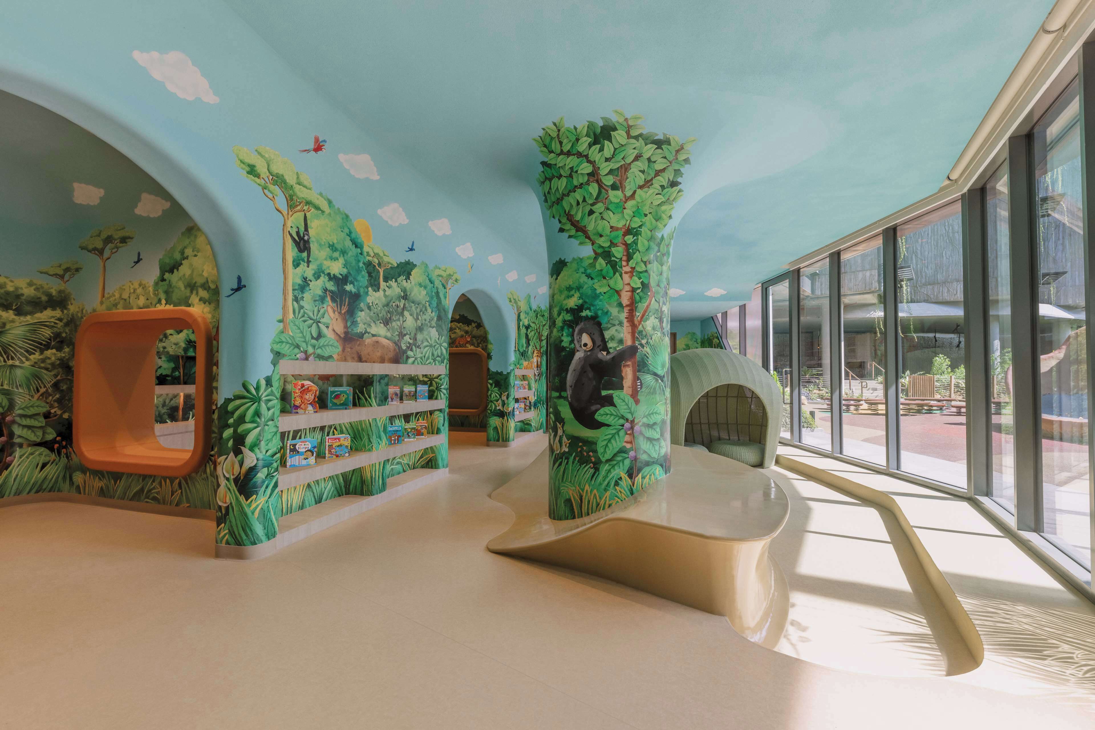 Ein Spielbereich für Kinder im Dschungel-Design, mit Kletterwand, Bücherregal und Rutsche.