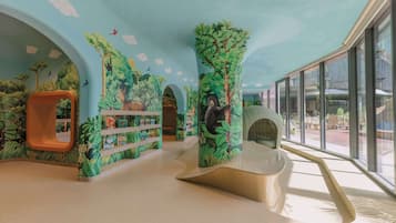 Ein Spielbereich für Kinder im Dschungel-Design, mit Kletterwand, Bücherregal und Rutsche.