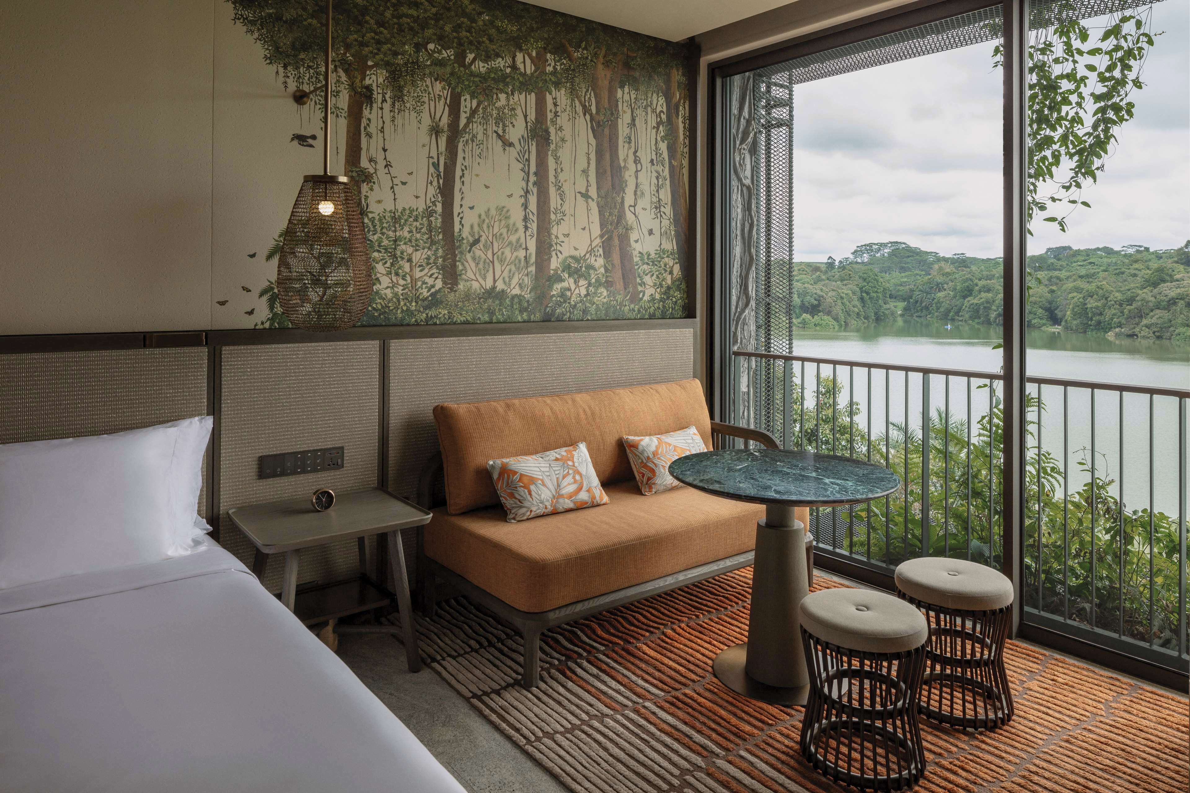 A hotel room with a bed, a sofa, a small table, and a view of a lake.