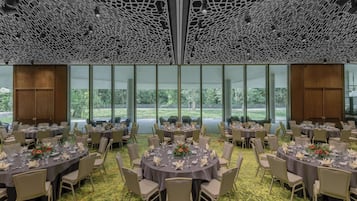 Ein Bankettsaal mit runden Esstischen, großen Fenstern mit Blick auf Grünflächen und einer Decke mit einem einzigartigen geometrischen Muster.
