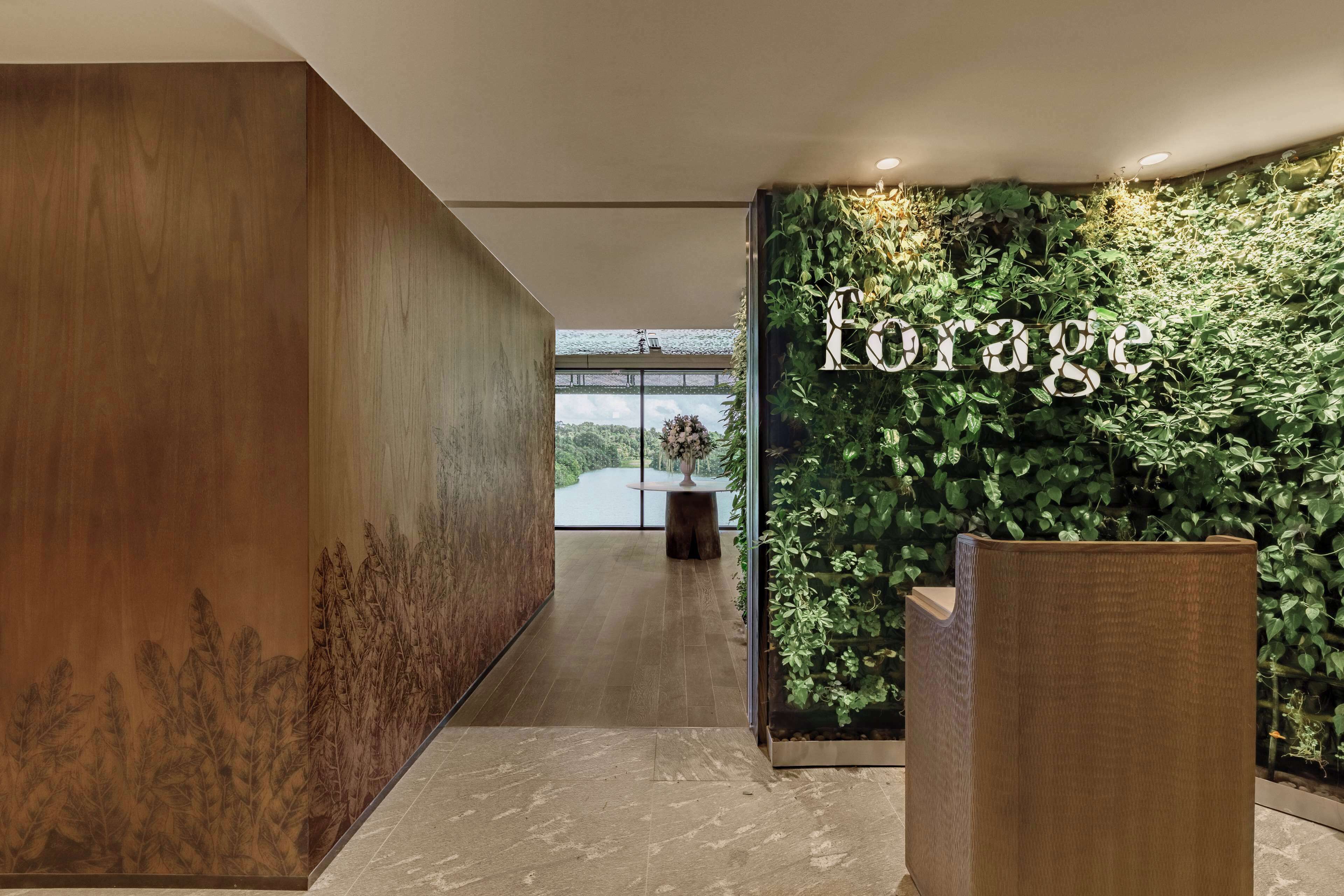 A reception area with a wooden wall, a green wall with a 'Forage' sign, and a view of a lake through large windows.