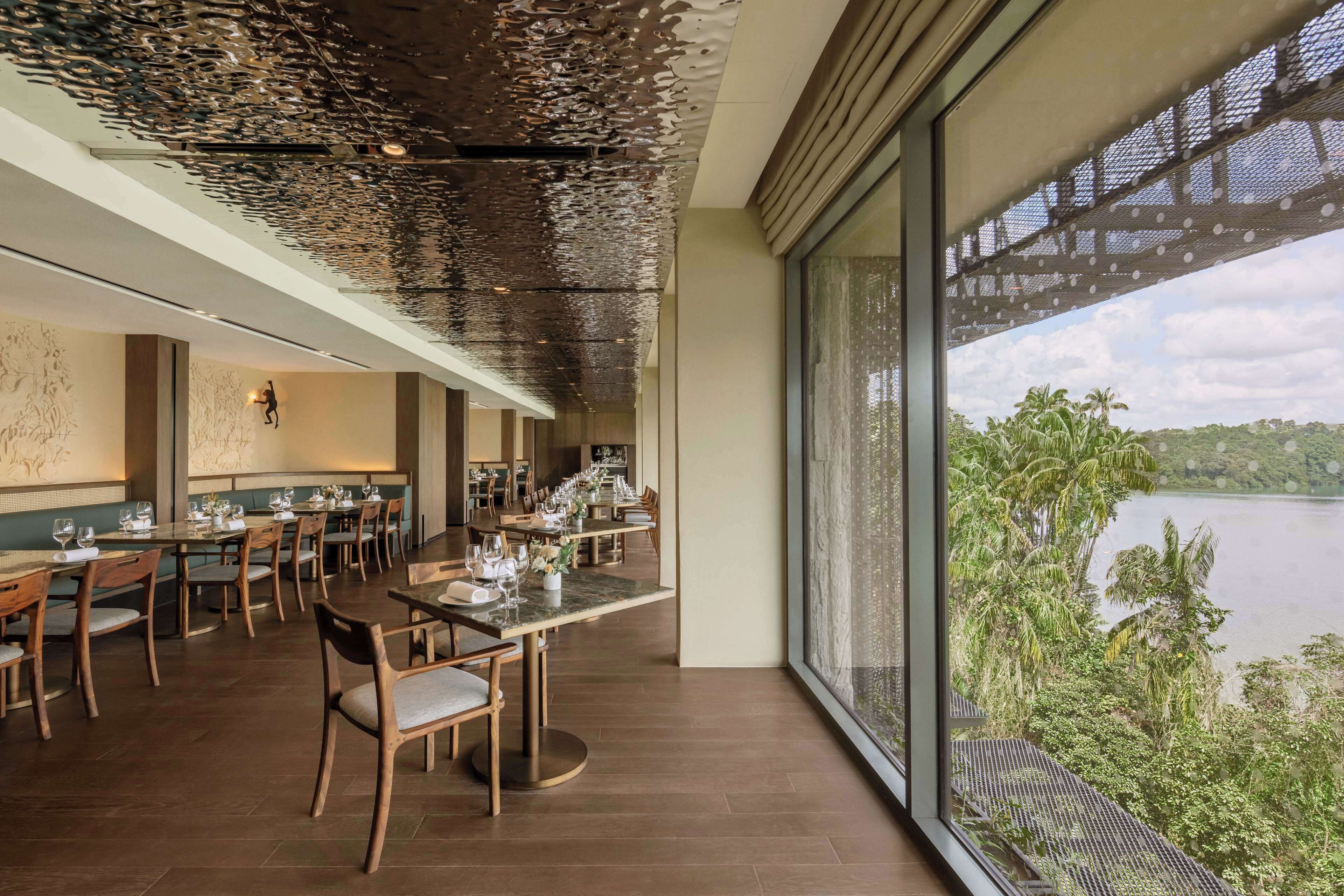 A restaurant with a long dining table, chairs, and a view of a lake.