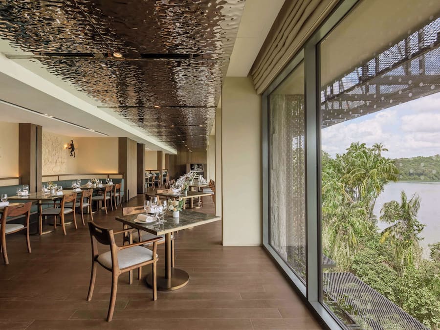 Un restaurante con una larga mesa de comedor, sillas y vistas a un lago.